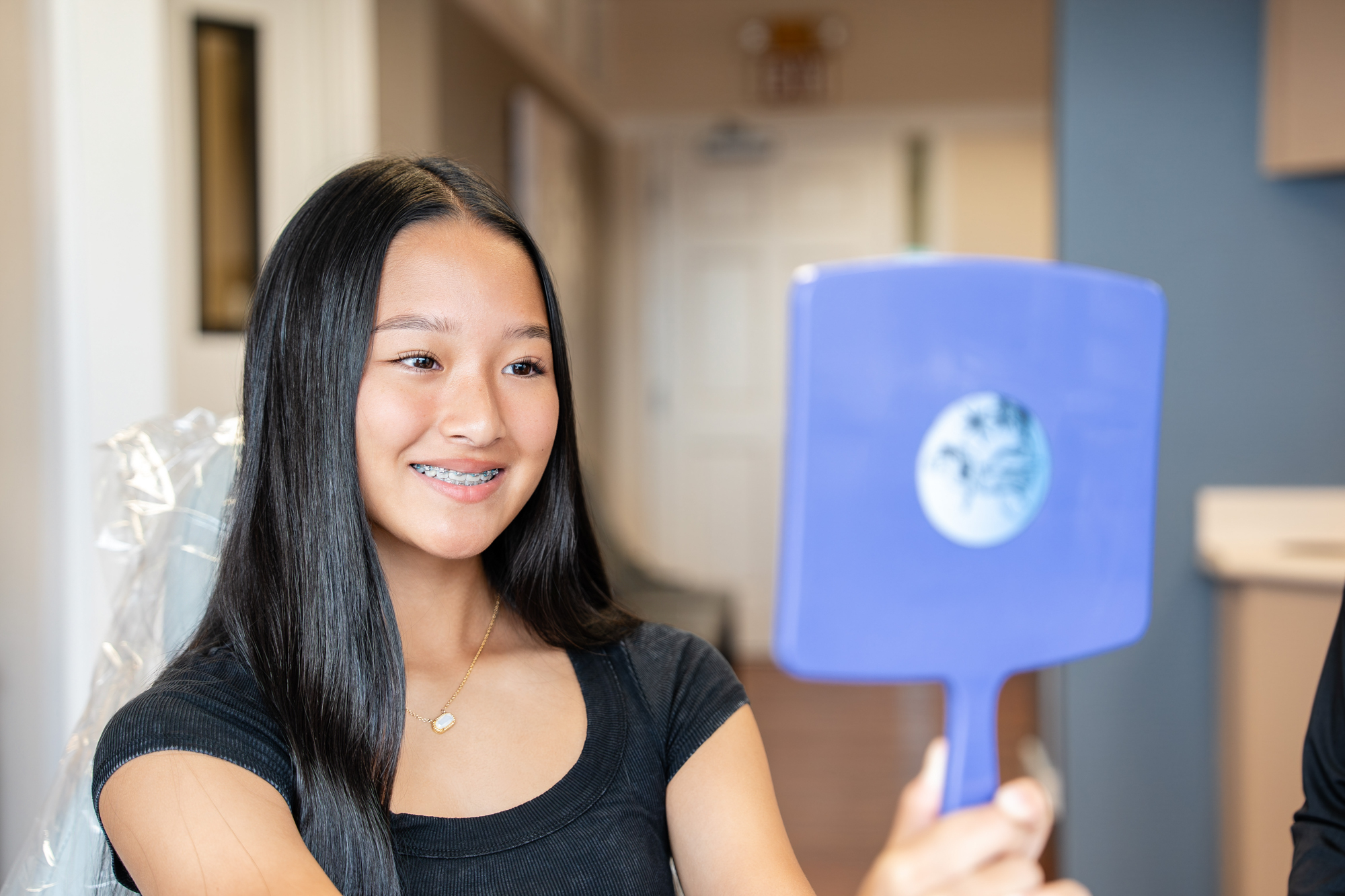 Smiling Maui Orthodontics patient with braces examining her teeth in a mirror.