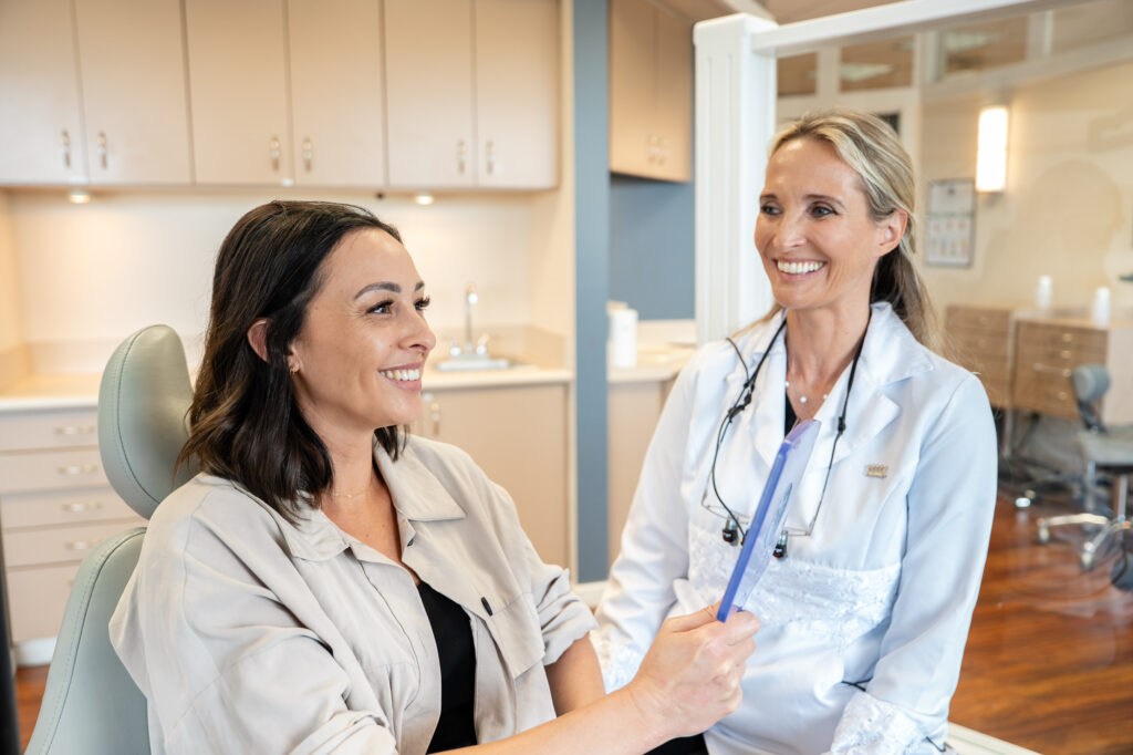 Dr. Aurelia Bonham, orthodontist at Maui Orthodontics, smiles with a patient in the treatment chair as she reviews the patient’s smile in a hand mirror.
