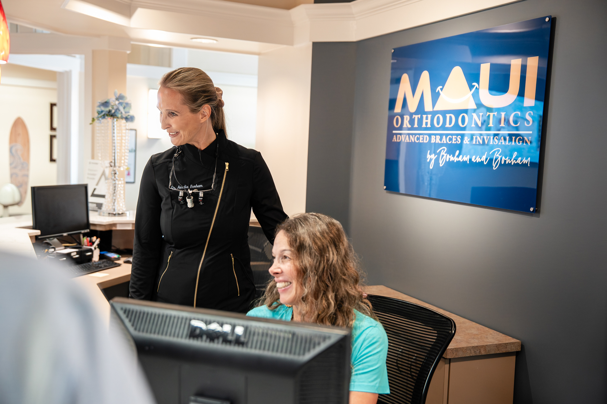 Dr. Aurelia Bonham smiling with a patient in front of the Maui Orthodontics logo wall at the Kihei orthodontist office